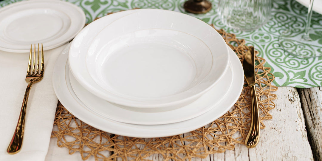 Luna Italian dinnerware place setting with layered white plates on a woven placemat with gold flatware.