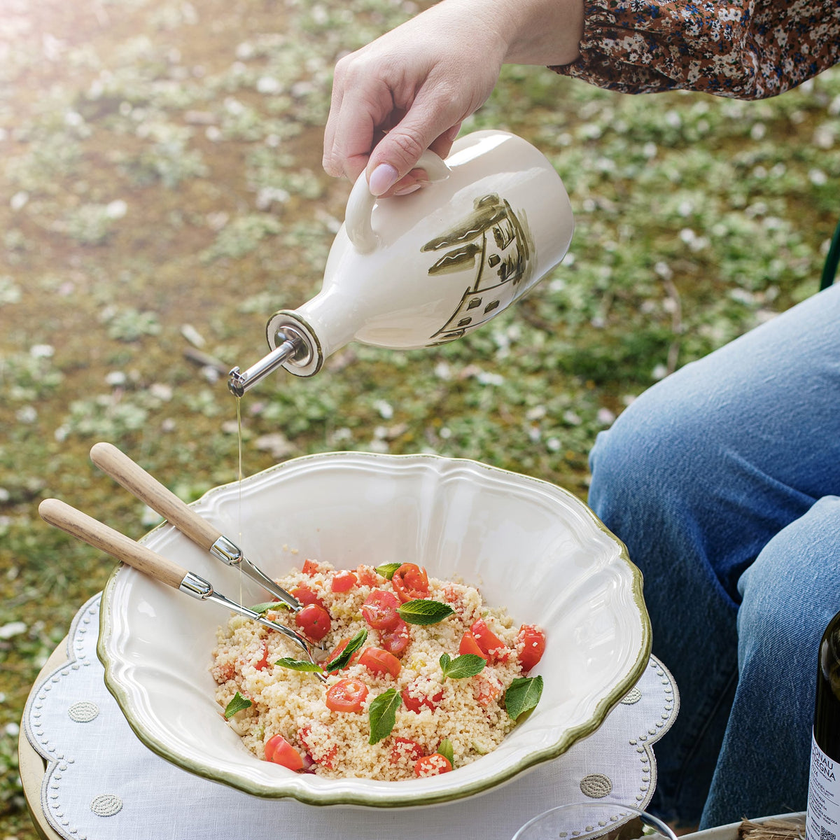 Person pouring olive oil over a salad in an outdoor setting
