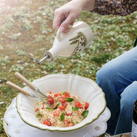Person pouring olive oil over a salad in an outdoor setting